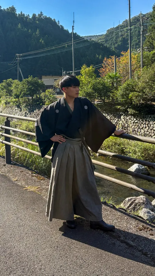 紋付袴姿で、山あいの川沿いに立つ香園 紳瑛
